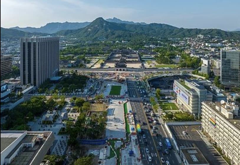Daytime aerial view of Gwanghwamun Square with Gyeongbokgung Palace and Bukhansan Mountain in the distance