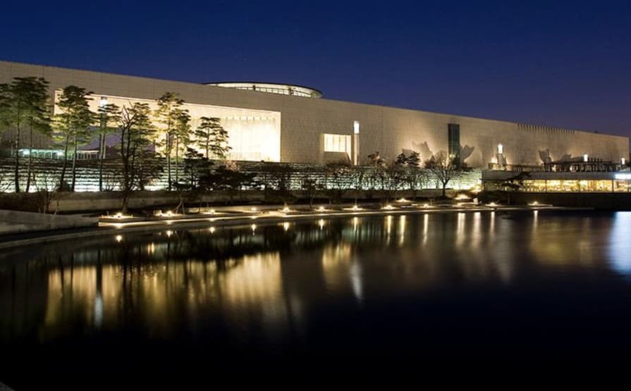 The illuminated National Museum of Korea building at night reflected in the still pond in front of it