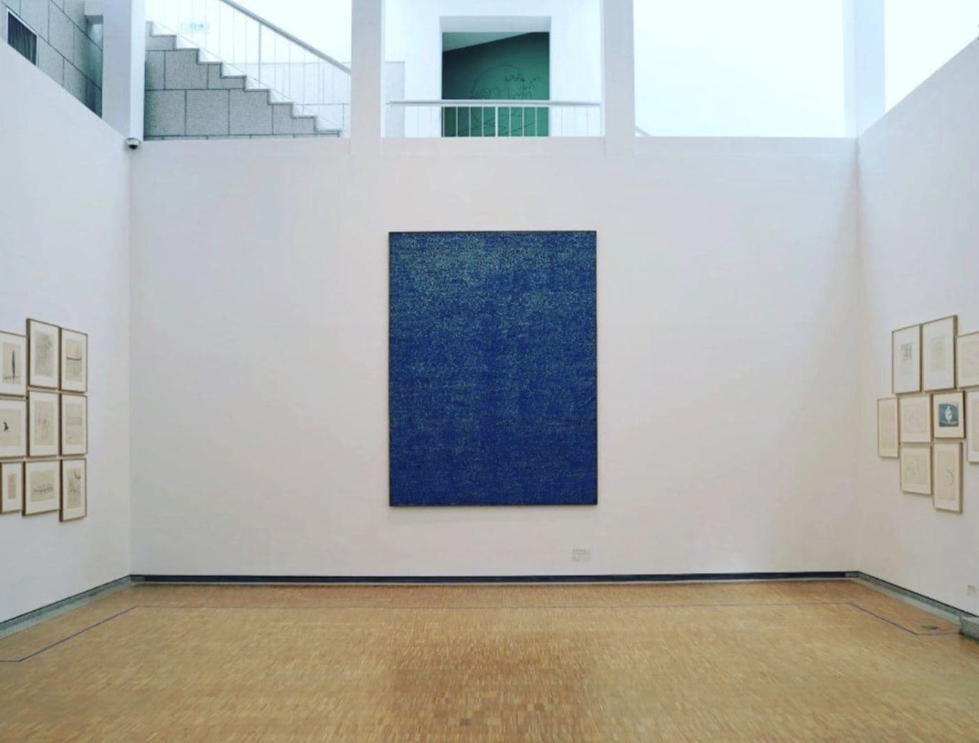 A Whanki Museum gallery interior with a large blue dot painting centered on a white wall, flanked by framed drawings